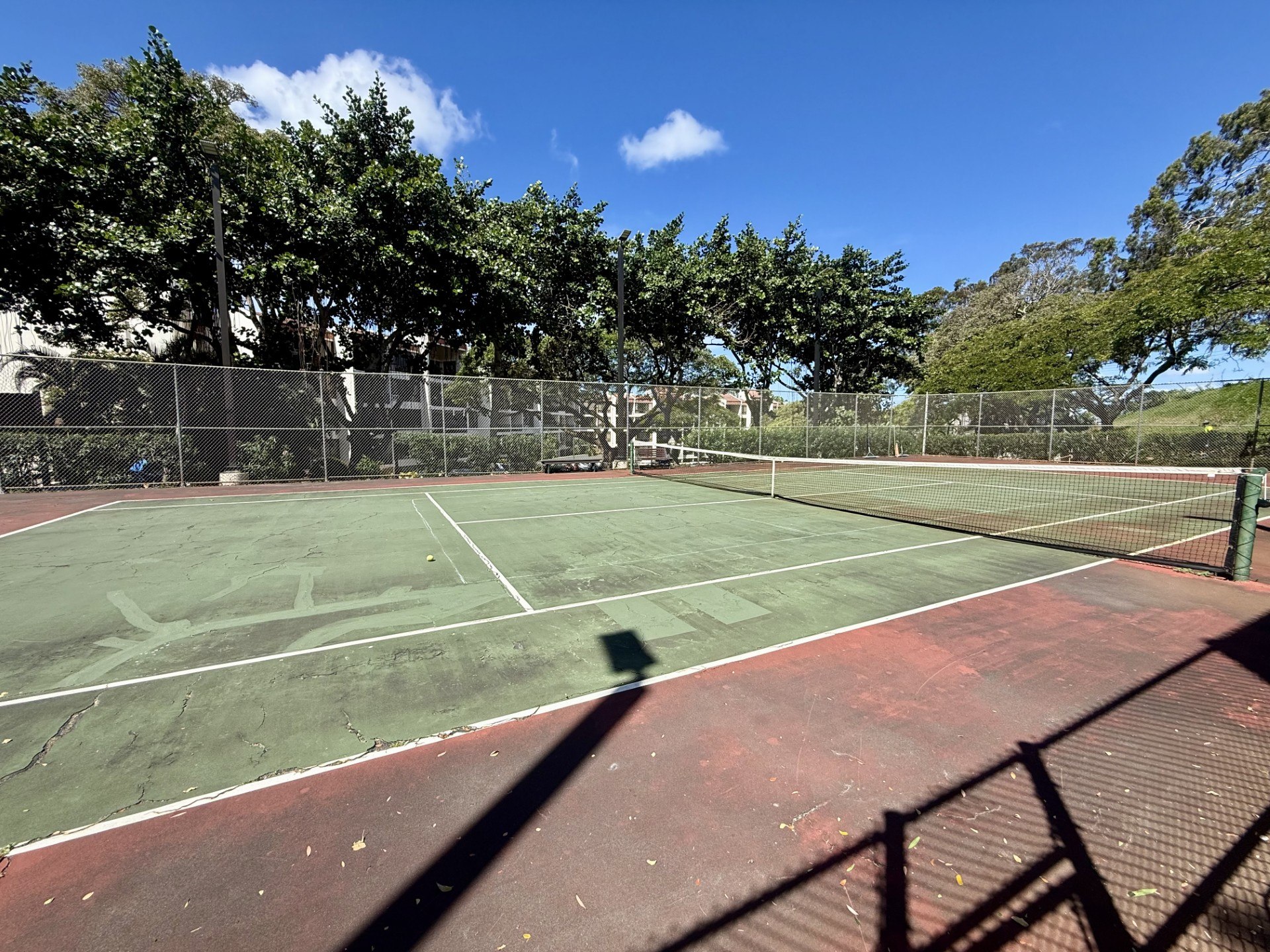 A tennis court with a green net and a red surface.